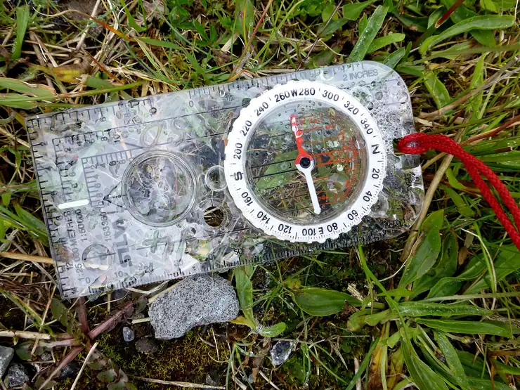 Transparent hiking compass resting on grass beside a small rock