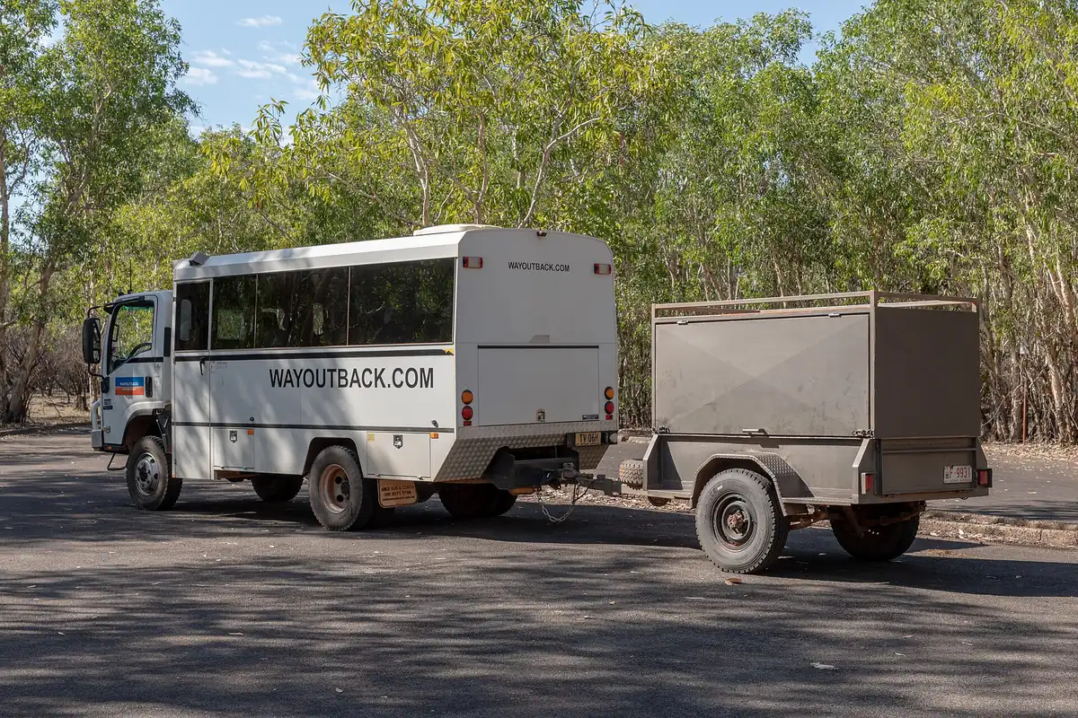 Truck towing a trailer parked beside trees on a paved lot