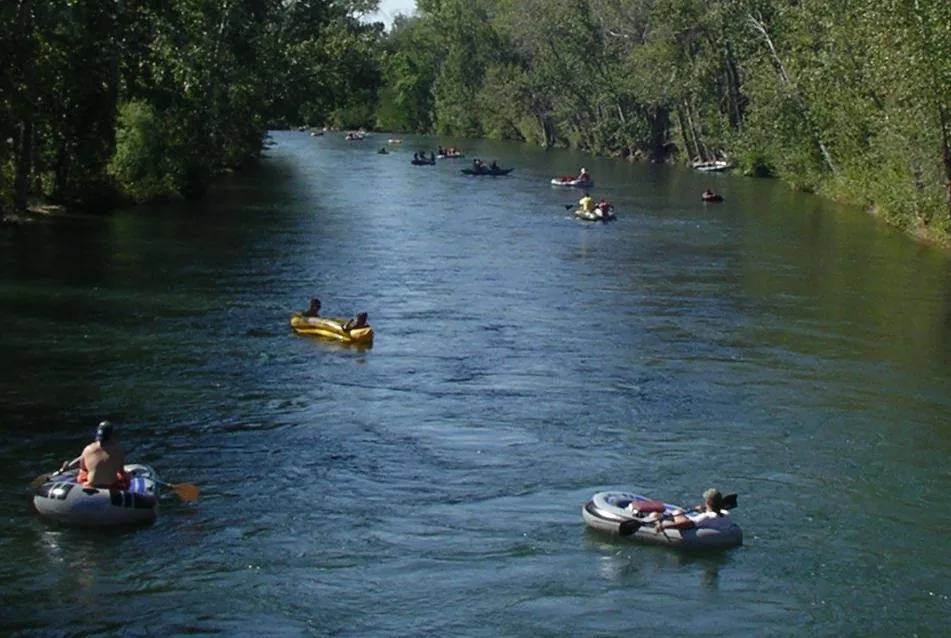 People floating down the tree-lined Boise River in rafts on a sunny day